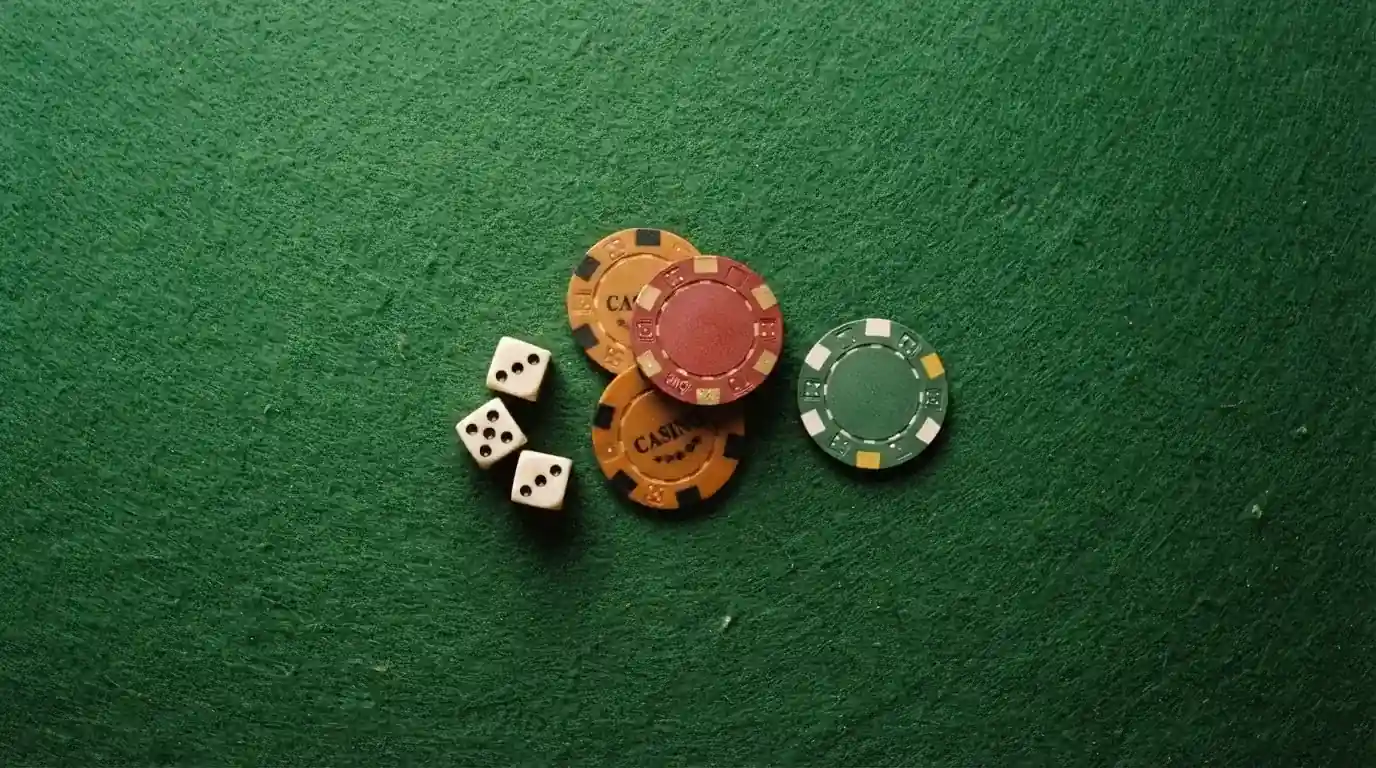 Vista cenital de fichas de casino y dados sobre una mesa de fieltro verde bajo luz suave.